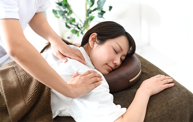 肩を揉むマッサージを受けている若い女性の画像