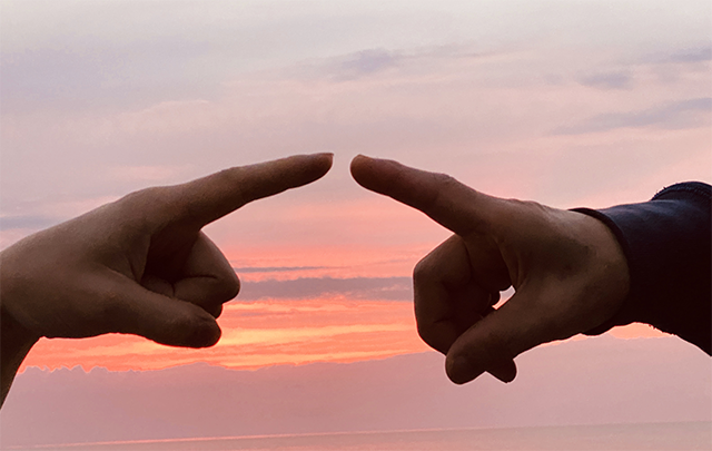 ゆい日を背景に親子が指と指を合わせようとするサイン（伝達）を互いに送る画像