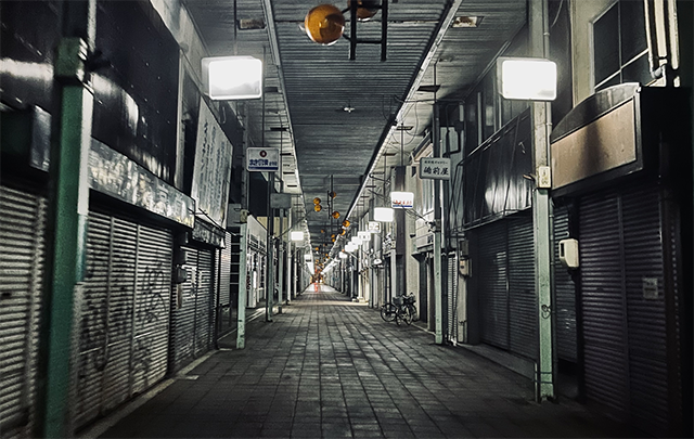 閑散として照明も暗い寂れた商店街のシャッター通りの暗いイメージ画像