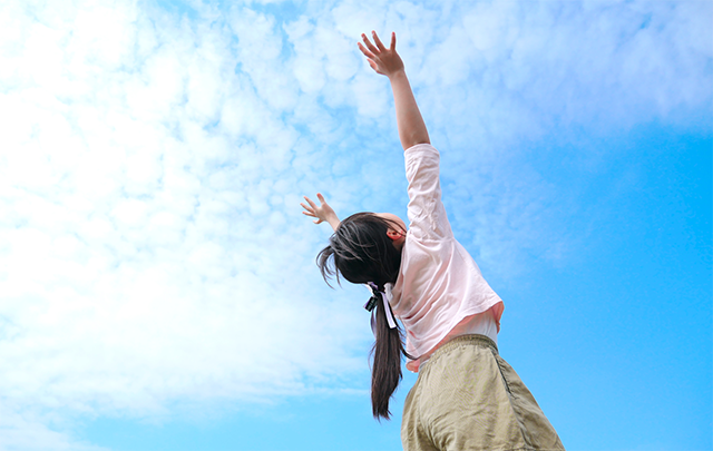 青空に向かって両手を伸ばし、日光浴を楽しむ少女の画像