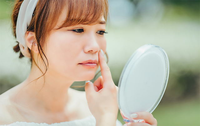 肌荒れを鏡で確認する若い女性の画像